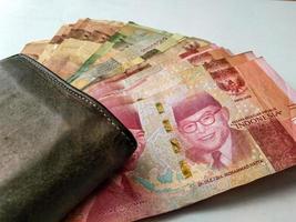 several rupiah bills with a brown wallet and a white background photo