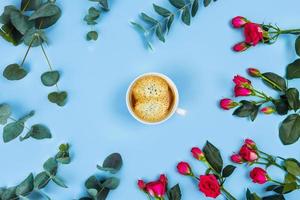 taza de café por la mañana y hermosas rosas con ramitas de eucalipto sobre fondo azul, vista superior. foto