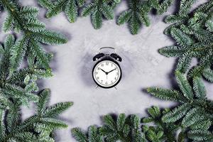 Black clock on gray concrete background surrounded by Christmas branches. photo