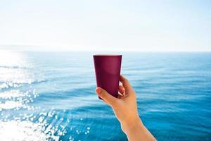 Hand with cup of coffee on a background of blue sea. photo