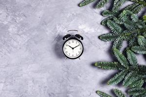 Black clock on grey concrete background with Christmas branches. photo