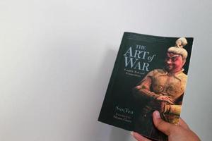 West Java, Indonesia on July 2022. A hand is holding a book called The Art of War by Sun Tzu. photo