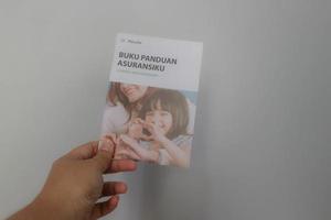 West Java, Indonesia on July 2022. A hand holding Manulife's Insurance Handbook for life and health insurance photo