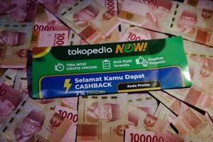 Jakarta, Indonesia in December 2022. A Tokopedia Now flyer above several hundred thousand rupiah notes scattered around. photo