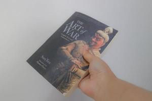 West Java, Indonesia on July 2022. A hand is holding a book called The Art of War by Sun Tzu. photo