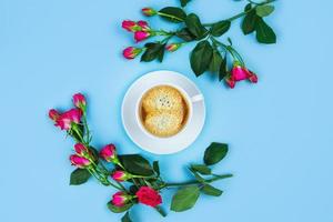 taza de café de la mañana y hermosas rosas sobre fondo azul, vista superior. foto