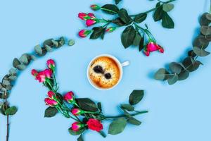 taza de café por la mañana y hermosas rosas con ramitas de eucalipto sobre fondo azul. foto