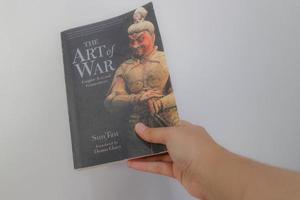 West Java, Indonesia on July 2022. A hand is holding a book called The Art of War by Sun Tzu. photo