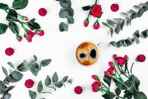 taza de café por la mañana con hermosas rosas y ramas de eucalipto sobre fondo blanco. foto