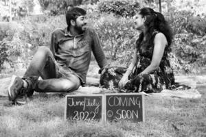 Indian couple posing for maternity baby shoot. The couple is posing in a lawn with green grass and the woman is falunting her baby bump in Lodhi Garden in New Delhi, India photo