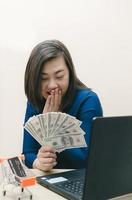 Smart woman in blue work clothes holds several banknotes in her expressions of joy. The concept of e-commerce online shopping. or doing business online. photo