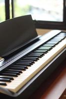 Black piano keyboard with white keys against window interior background photo