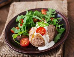 Baked potato filled with sour cream, arugula and tomatoes photo