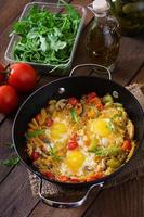 Fried eggs with vegetables in a frying pan on a wooden background photo
