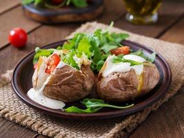 Baked potato filled with sour cream, arugula and tomatoes photo