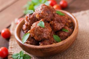 Meatballs in sweet and sour tomato sauce and basil in a wooden bowl photo