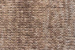Knitted background. Knitted wallpaper. Beige knitted fabric. Knitted texture. Soft material. Brown, beige and white handmade sweater close up photo. Cozy background. Knitwear detail. Woolen cloth. photo