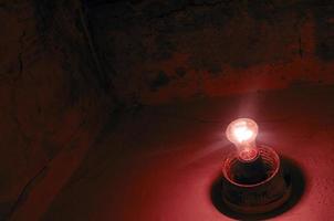 Anxiety concept. Alert symbol. Alarm lamp. Red bulb in dark red room.  Red lightbulb and dirty walls. Dark scary room with cracked walls. Danger and fear concept. Alarm in an abandoned house. photo