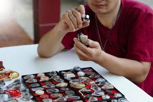 Closeup man's hands hold Buddha amulet and magnifying glass to check details and figure of object. Concept, faith, belief in holy and luck for Buddhists.  Colleting amulet as hobbies, exchange, trade. photo