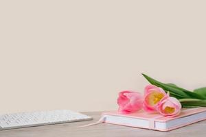 Workspace with keyboard, pink diary and pink tulips on wooden background. Space for text photo