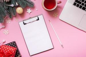 Blank note paper on tablet and Cristmas New Year work table decoration top view, flat lay on pink background photo