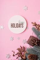 felices fiestas texto y adornos navideños vista superior sobre fondo rosa. formato vertial de la tarjeta de felicitación de navidad foto