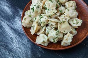 Traditional russian pelmeni or ravioli, dumplings with meat on wood black background. Russian food and russian kitchen concept. photo