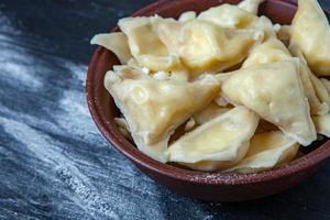 Traditional russian pelmeni or ravioli, dumplings with meat on wood black background. Russian food and russian kitchen concept. photo