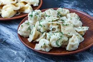 Traditional russian pelmeni or ravioli, dumplings with meat on wood black background. Russian food and russian kitchen concept. photo