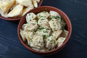 Traditional russian pelmeni or ravioli, dumplings with meat on wood black background. Russian food and russian kitchen concept. photo