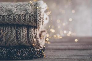 Stack of cozy winter or autumn knitted sweaters and garland lights on wooden background. Warm Cozy Concept photo