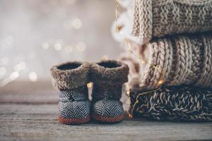 Stack of cozy winter knitted sweaters, cute small boots and christmas ornaments on a blurred background with bokeh. photo
