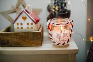Close-up of home christmas decor - burning candle, ceramic house, jar with natural cone. photo
