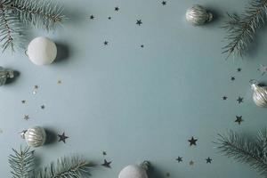 Winter holidays concept. Top view photo of fir tree branches and festive decoration on blue background with empty space in the middle for text