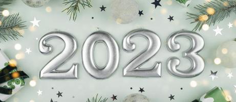 Numbers of year 2023 made by candles. Fir tree, gift box, holiday decoration on light green background. Christmas postcard. Happy New Year 2023 card concept. Flat lay, top view. Banner photo