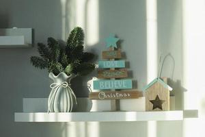 Winter decor composition on white shelf- spruce branches in vase, wooden tree decor and candlestick photo