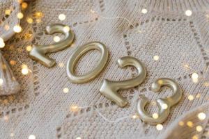 Numbers 2023 made of golden number on beige knitted sweater as background. Happy New Year 2022, Christmas, cozy holiday concepts. photo