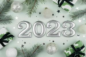 Numbers of year 2023 made by candles. Fir tree, gift box, holiday decoration on light green background. Christmas postcard. Happy New Year 2023 card concept. Flat lay, top view photo