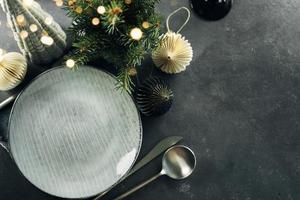 Christmas table setting with empty craft ceramic plate and silver cutlery on dark stone background. Top view. photo