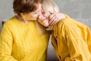 Mother hugging her adult daughter while sitting on the couch. Family relaltionships photo