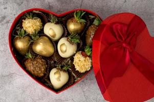 vista superior de la caja en forma de corazón con una variedad de fresas cubiertas de chocolate sobre un fondo gris. San Valentín, concepto del día de la madre foto