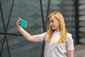 Young blond woman making selfie on smartphone for her followers. Young influencer girl. Popularity in internet, friends online. Beautiful girl making content for her social media account. photo