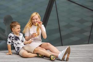 Happy blond woman and little boy sitting on terrace and eating sweets. Mother and son enjoy time together. Positive young mom playing, spending time with her cute child, laughing, having fun. Family. photo