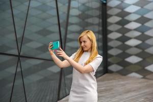 Young blond woman making selfie on smartphone for her followers. Young influencer girl. Popularity in internet, friends online. Beautiful girl making content for her social media account. photo