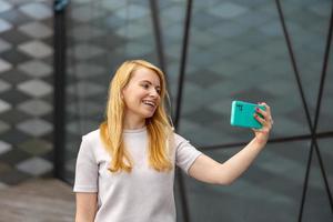 Young blond woman making selfie on smartphone for her followers. Young influencer girl. Popularity in internet, friends online. Beautiful girl making content for her social media account. photo