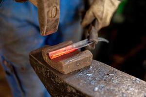 Close up view of heated metal and anvil. The blacksmith in the production process of metal products handmade in the forge. Blacksmith forging metal with a hammer. Metal industry, old profession. photo