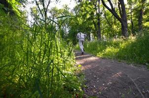 A young guy in a gray sports suit runs along the path among the photo