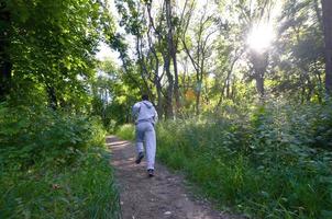 A young guy in a gray sports suit runs along the path among the photo