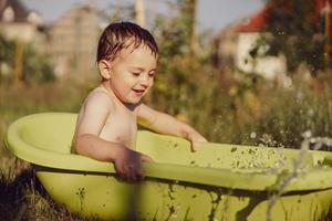 Cute little boy bathing in tub outdoors in garden. Happy child is splashing, playing with water and having fun. Summer season and recreation. Staying cool in the summer heat. Water fun in backyard. photo