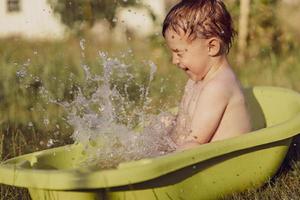 Cute little boy bathing in tub outdoors in garden. Happy child is splashing, playing with water and having fun. Summer season and recreation. Staying cool in the summer heat. Water fun in backyard. photo